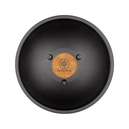 Back view of Novadrum 38 steel tongue drum in black matte, showing a wooden cover with engraved ‘NovaDrum’ branding, rubber feet, and black rope rim.