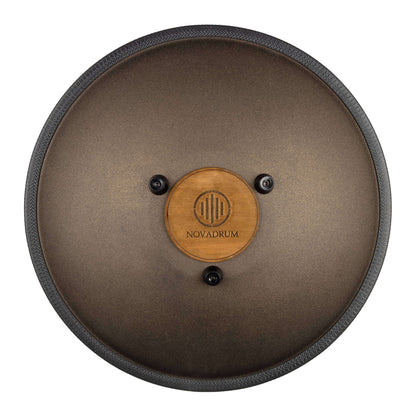 Back view of Novadrum 38 steel tongue drum in bronze matte, showing a wooden cover with engraved ‘NovaDrum’ branding, rubber feet, and black rope rim.