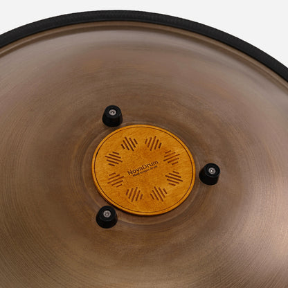 Close-up back view of Novadrum 48 big steel tongue drum in stainless steel, focusing on the wooden cover with engraved ‘NovaDrum’ branding, rubber feet, and black rope rim.