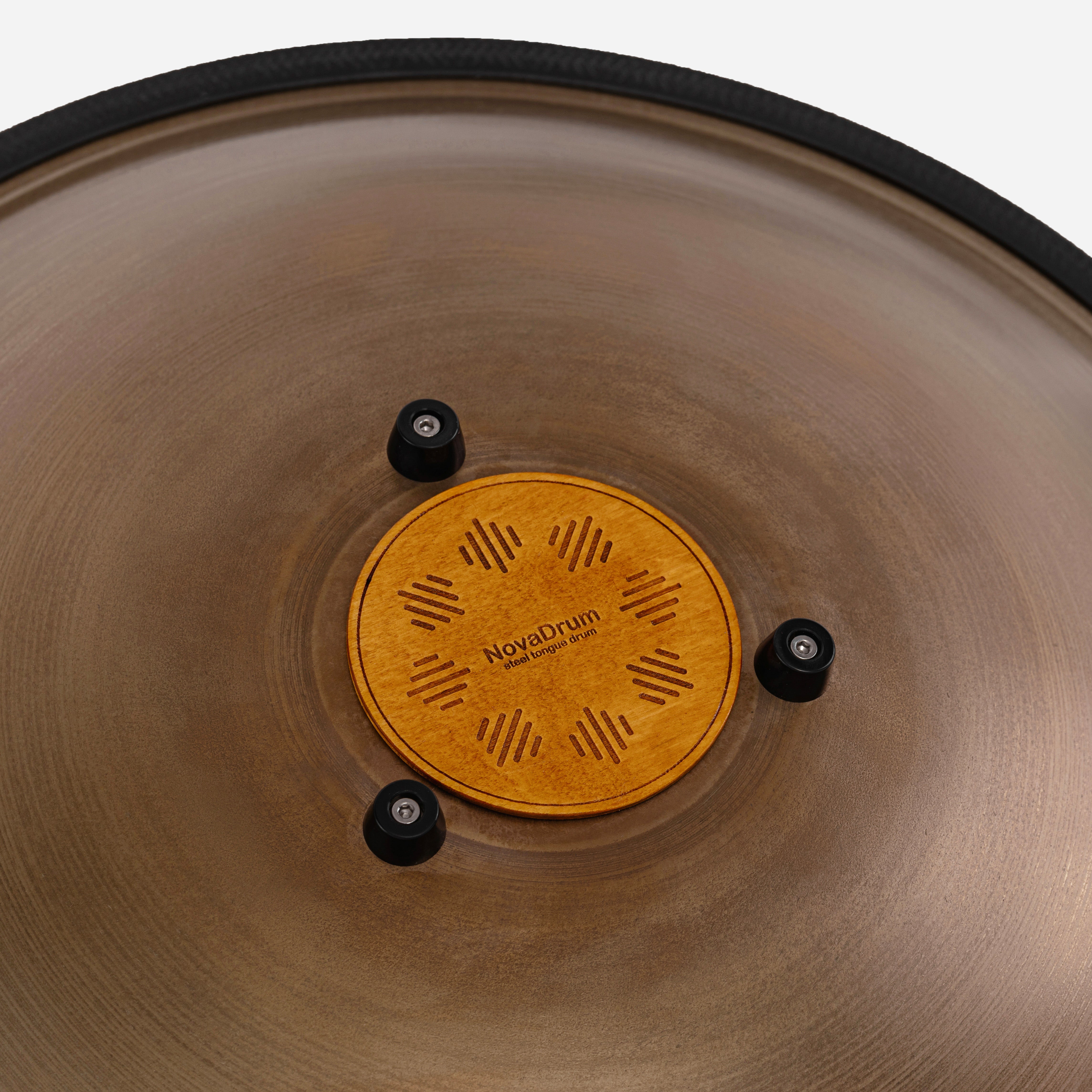 Close-up back view of Novadrum 48 big steel tongue drum in stainless steel, focusing on the wooden cover with engraved ‘NovaDrum’ branding, rubber feet, and black rope rim.