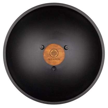 Back view of Novadrum 48 big steel tongue drum in black matte, showing a wooden cover with engraved ‘NovaDrum’ branding, rubber feet, and black rope rim.