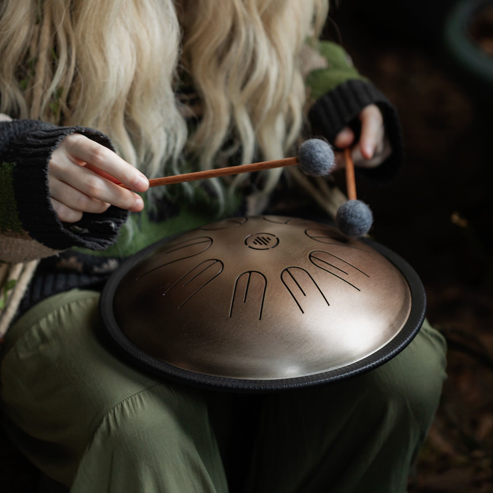 Person playing the Novadrum 28 steel tongue drum (also known as a steel tongue drum or tank drum) with padded mallets on their lap